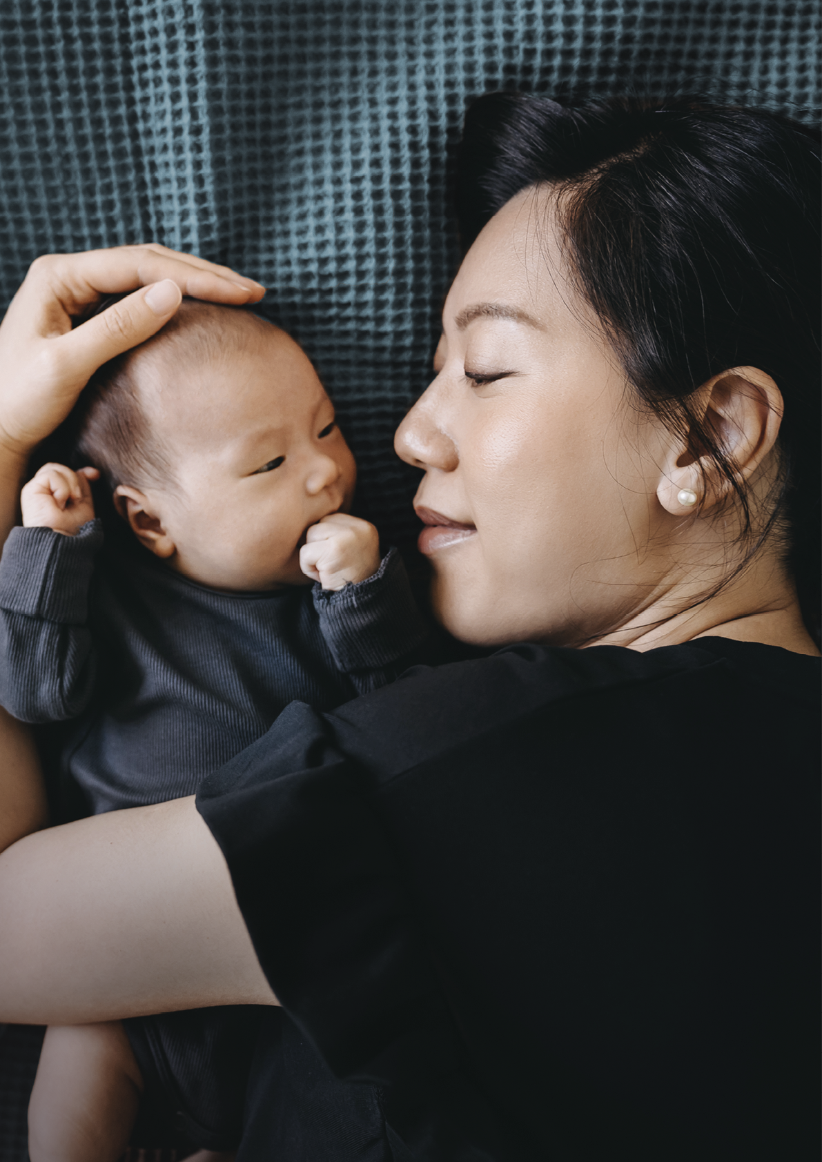 Loving and affectionate young Asian mother cuddling her newborn baby daughter on the bed. Precious moment of mother and daughter. Love, care and tenderness. Motherhood, parenthood concept