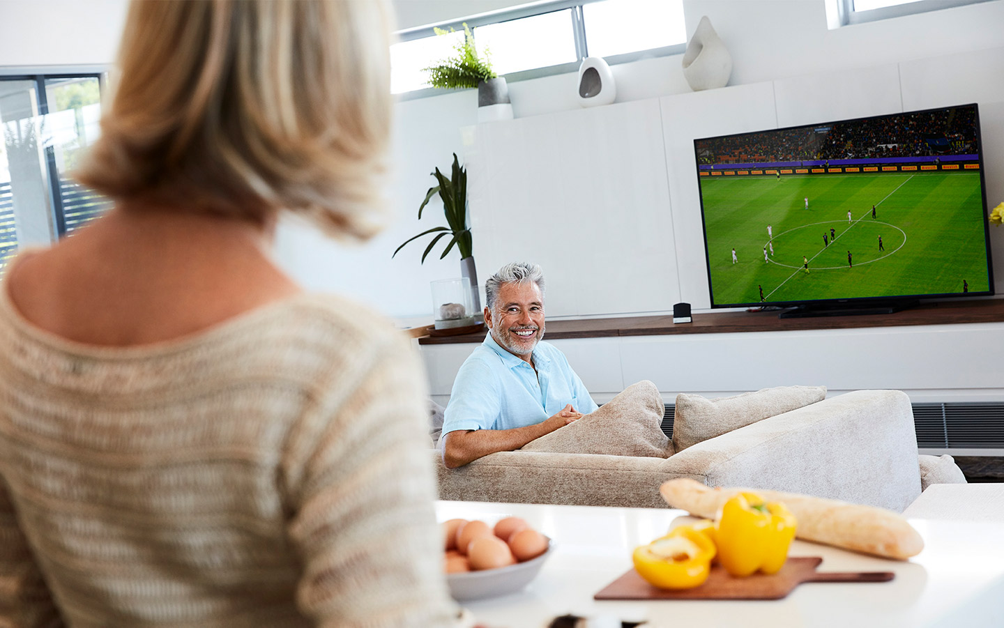 Homem adulto assistindo ao futebol na TV com o Cochlear Wireless TV Streamer
