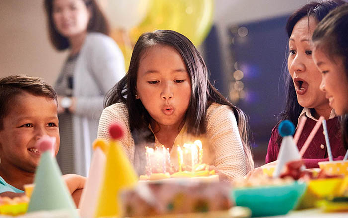 Menina com um implante coclear assoprando vela de aniversário com a família