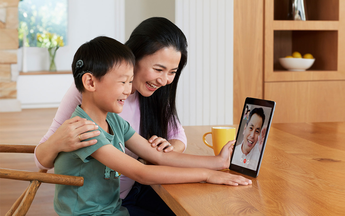 Rapaz asiático com o processador de som Nucleus conversando com seu pai via Facetime