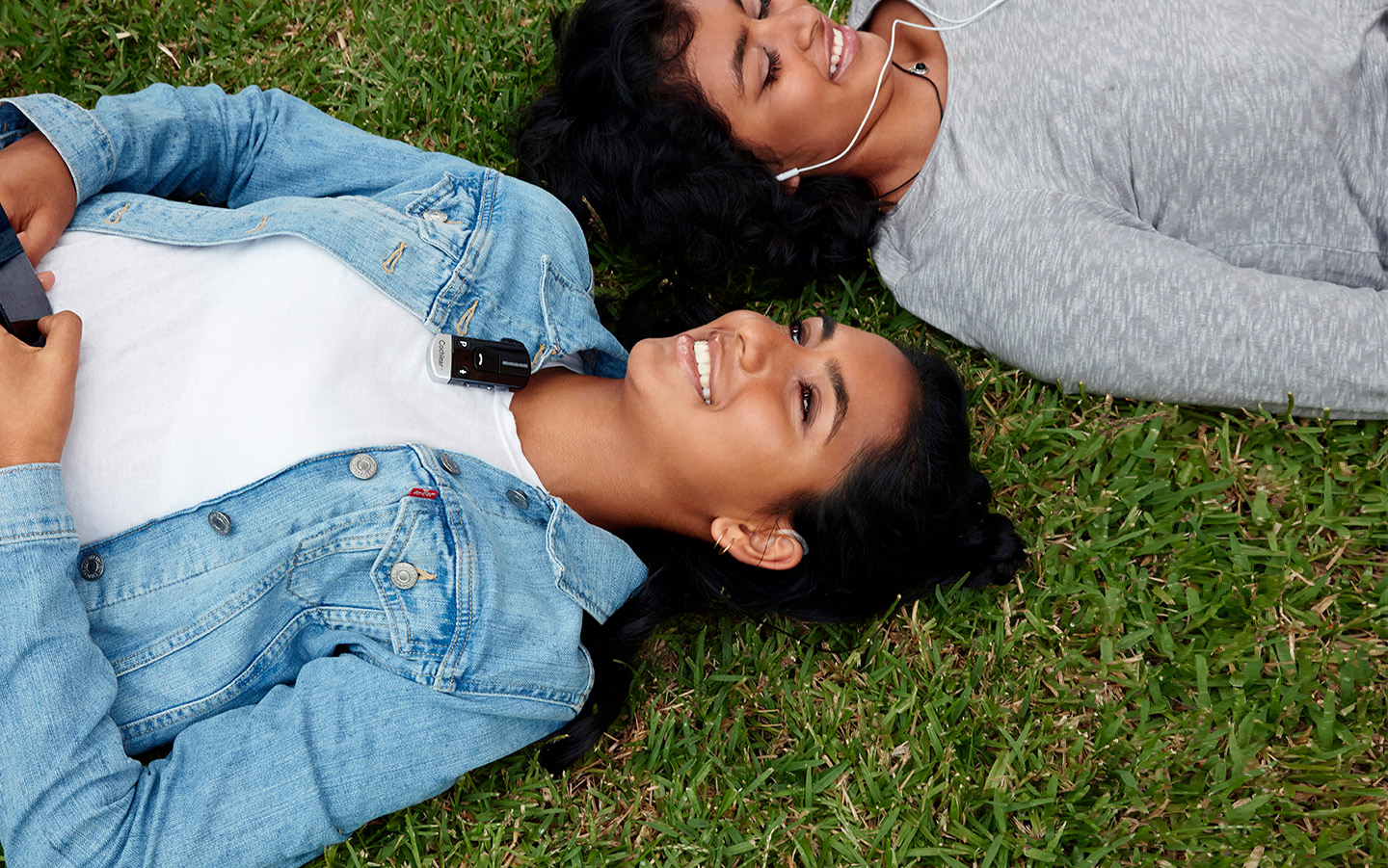 Amigas tendidas sobre el césped hablando con un minimicrófono